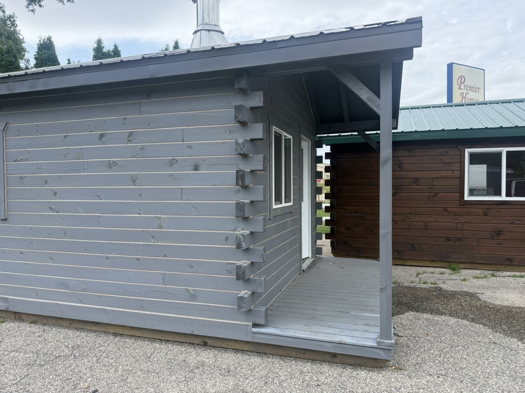 Exterior of the 12×28 square log cabin with gray stain and covered porch at the Tomah display lot