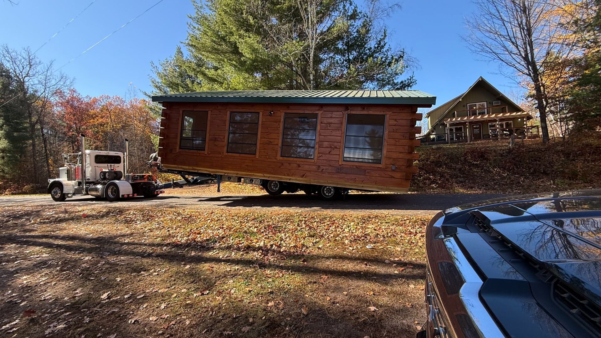 Single-level log cabin with green roof being delivered on trailer